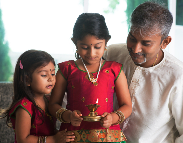 Indian children and adult in traditional sari celebrate diwali or deepavali. A little girl is holding an oil lamp during the festival of light.